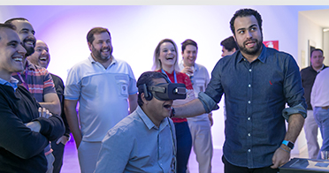 LATAM-whychoose-digital-ko 직원이 가상 현실 헤드셋을 착용한 한편, 이 직원의 반응을 지켜보는 다른 사람들